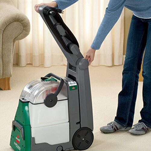 Person adjusting a carpet cleaner handle on a beige carpet.