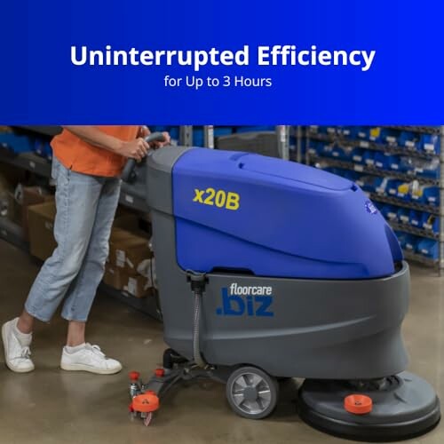 Person using a large floor cleaning machine in a warehouse setting.