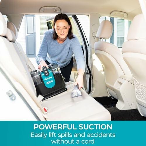 Person cleaning car seat with handheld vacuum cleaner.