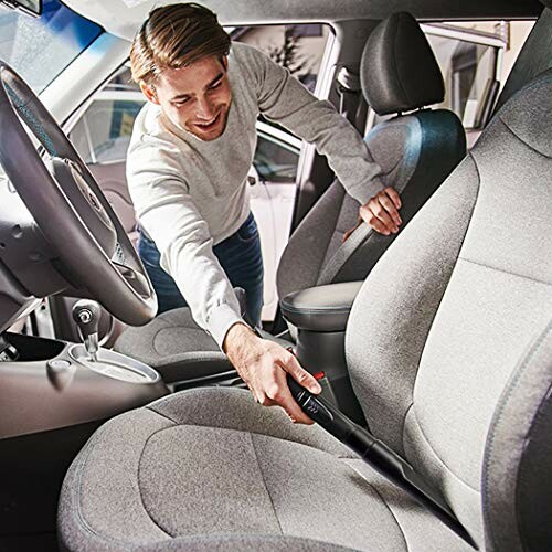 Man using a vacuum to clean car seats.