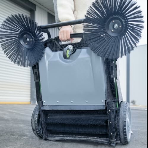 Person holding manual floor sweeper with rotating brushes