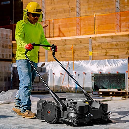 Worker using a concrete floor sweeper on a construction site.